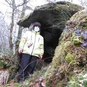 man in forest, standing under an outcrop, wearing yellow jacket and pandemic mask