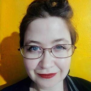 headshot of woman wearing glasses, smiling at camera on yellow background